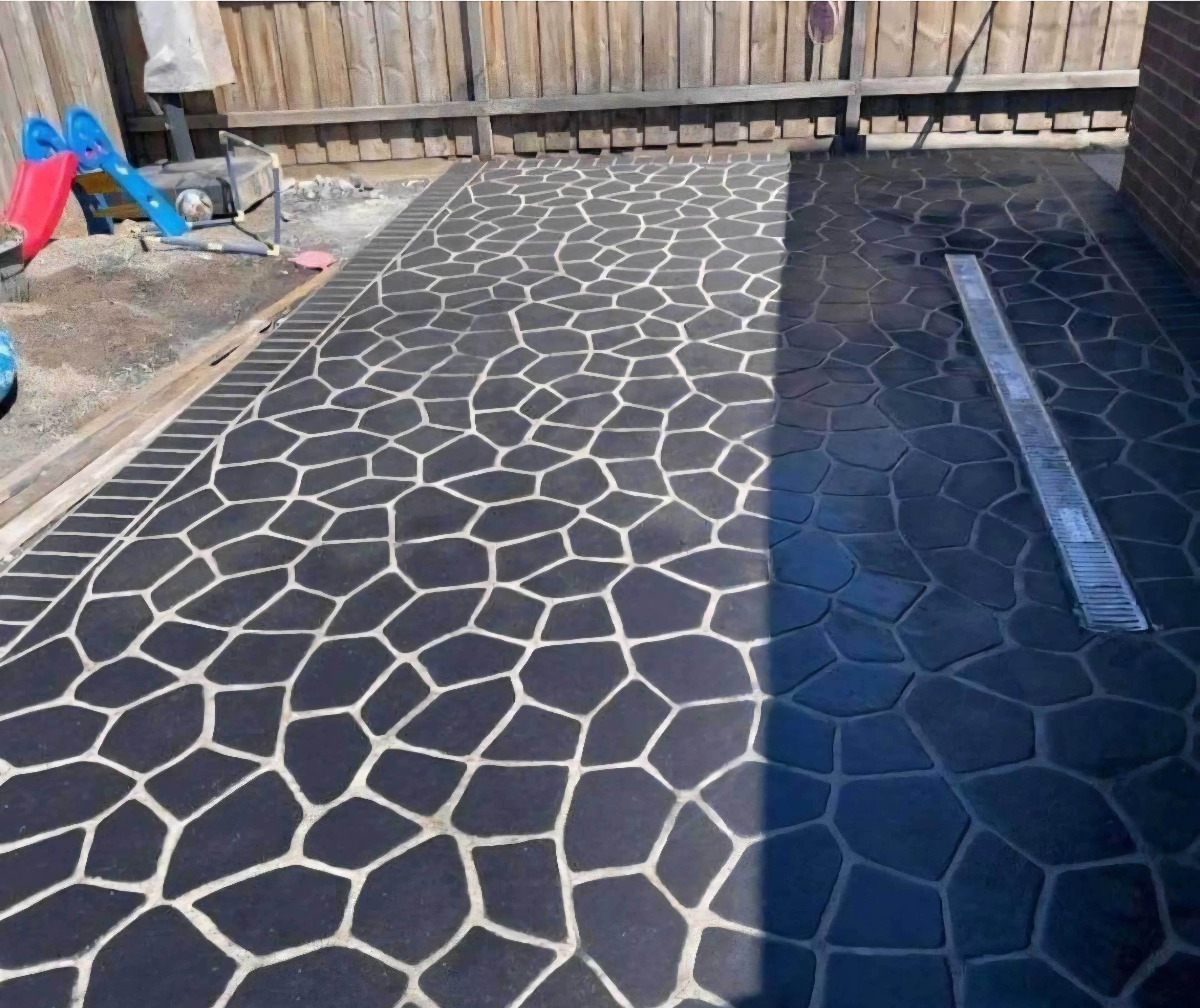 Charcoal crazy-paving pattern across a fenced backyard with a strip drain